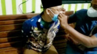 Seorang personel polisi membantu perbaiki posisi kacamata dan masker Wilson Lalengke saat kedua tangannya masih diborgol ke belakang